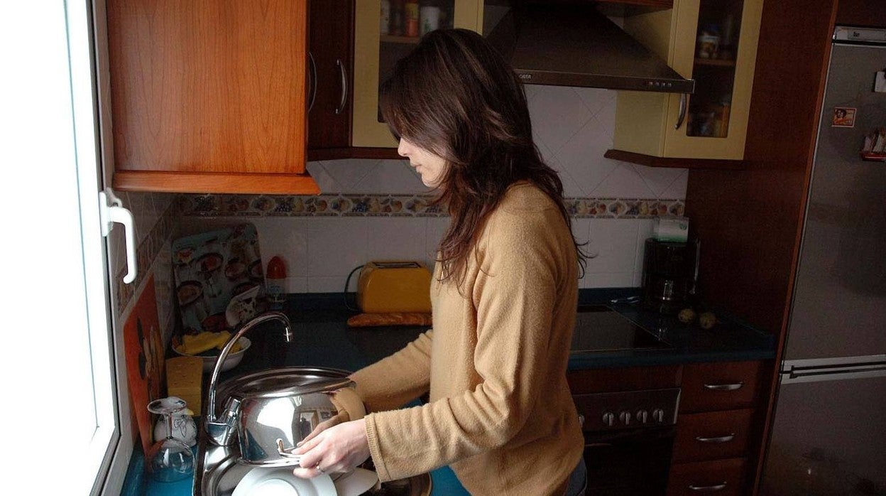 Una mujer friega los platos en la cocina de su casa