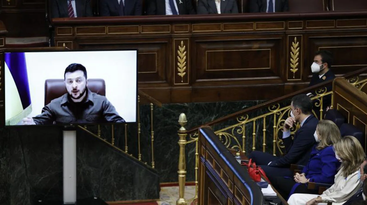 El presidente del Gobierno, Pedro Sánchez (3d), escucha la intervención por videoconferencia del presidente de Ucrania, Volodímir Zelensky en el pleno del Congreso