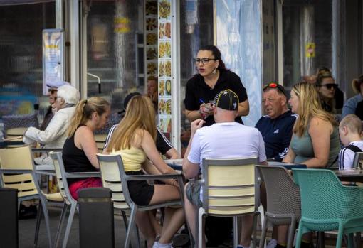 Una camarera atienda a turistas en la terraza de un bar en Benidorm