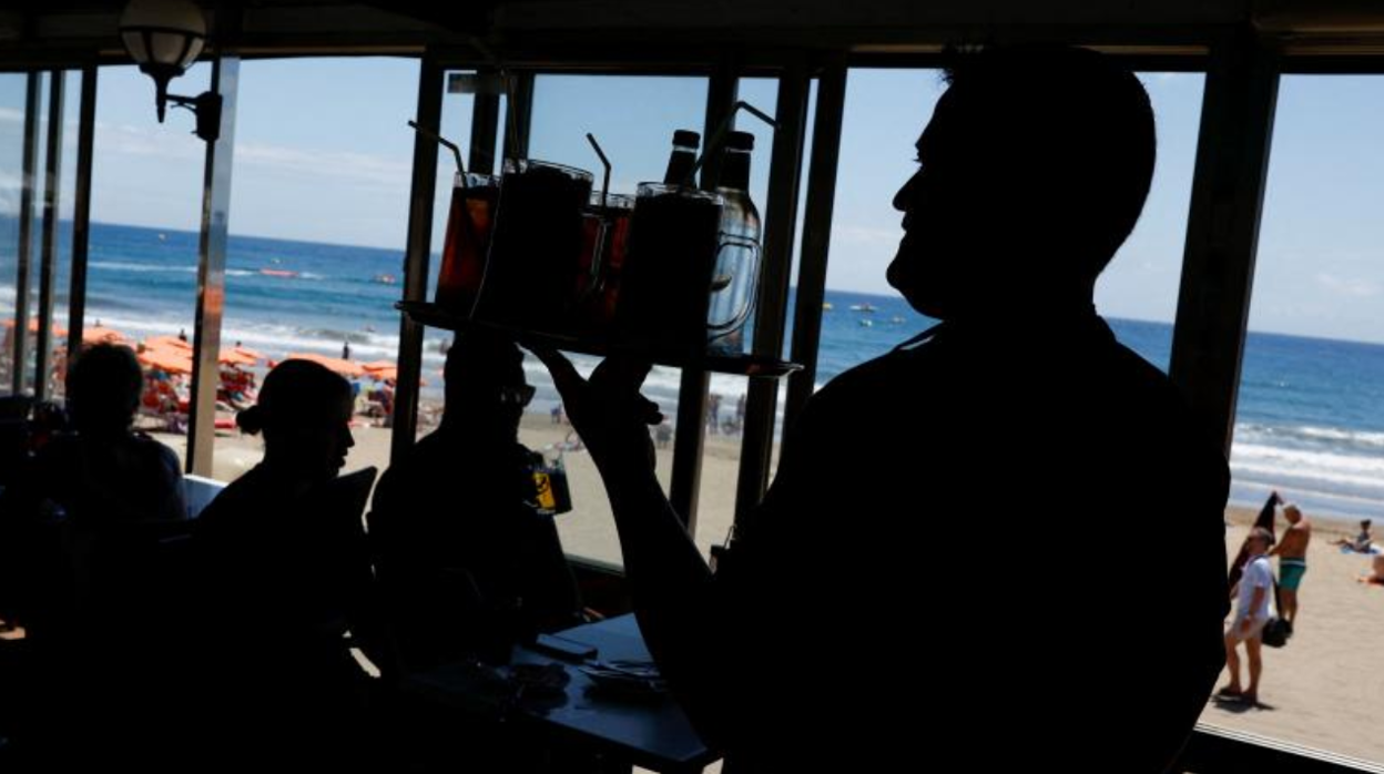 Un camarero lleva bebidas a una mesa n un local en Maspalomas