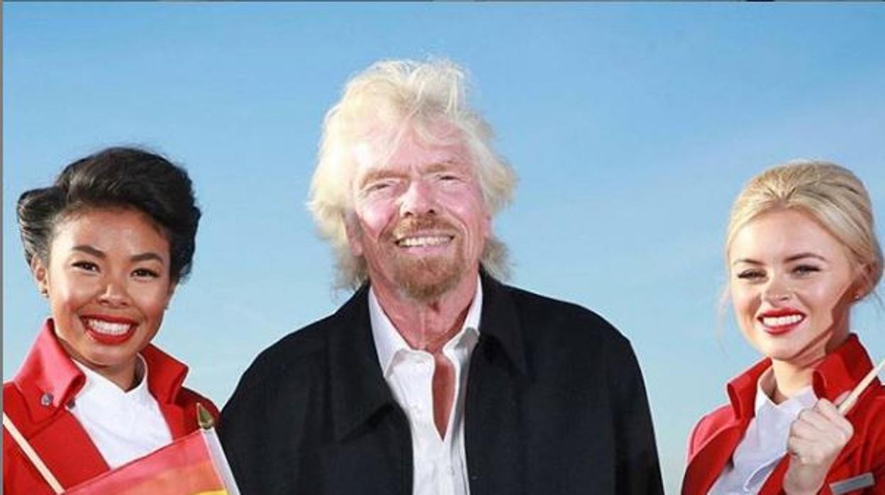 Richard Branson flanqueado por dos azafatas de la compañía