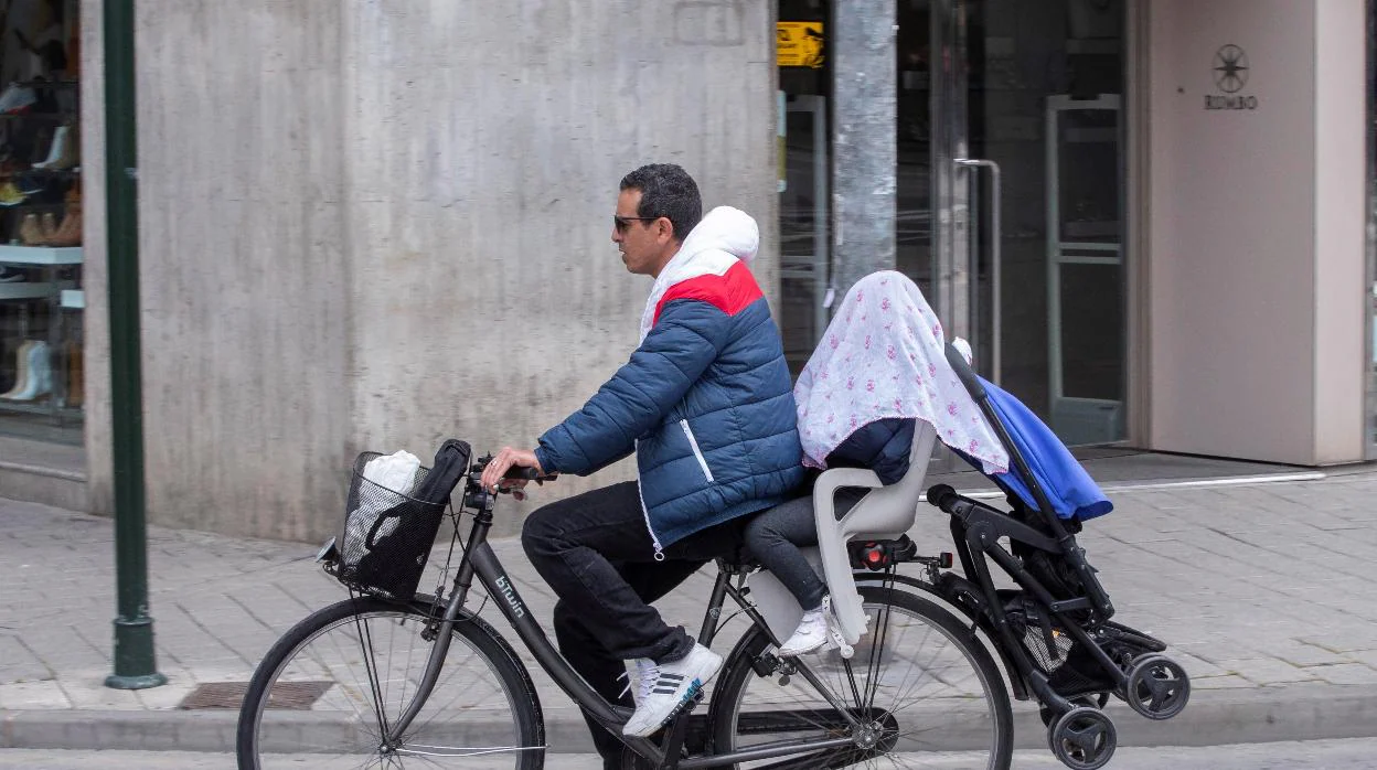 Un hombre lleva en bicicleta a su hijo tapado con una tela durante el estado de alarma