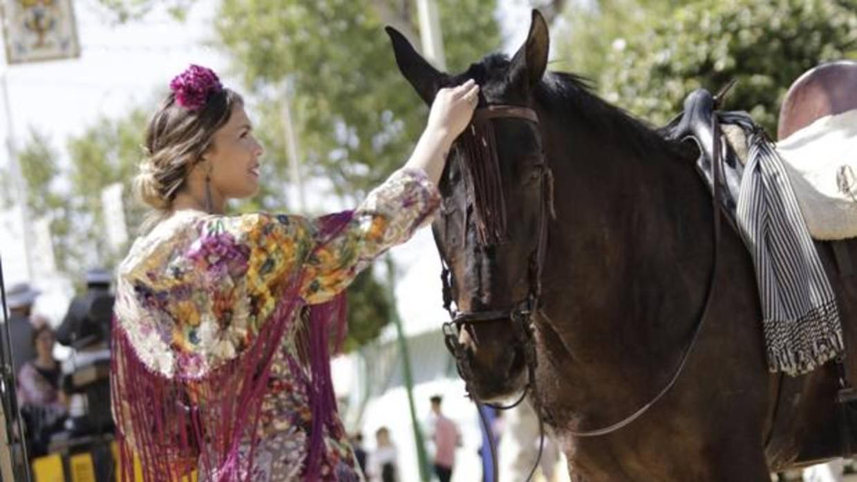 Una chica vestida de gitana acaricia las crines de un caballo