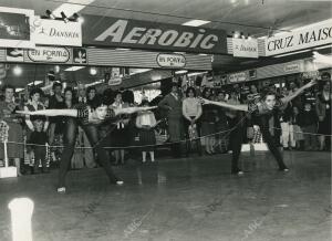 En la fotografía dos jóvenes realizan ejercicio mientras el público observa...