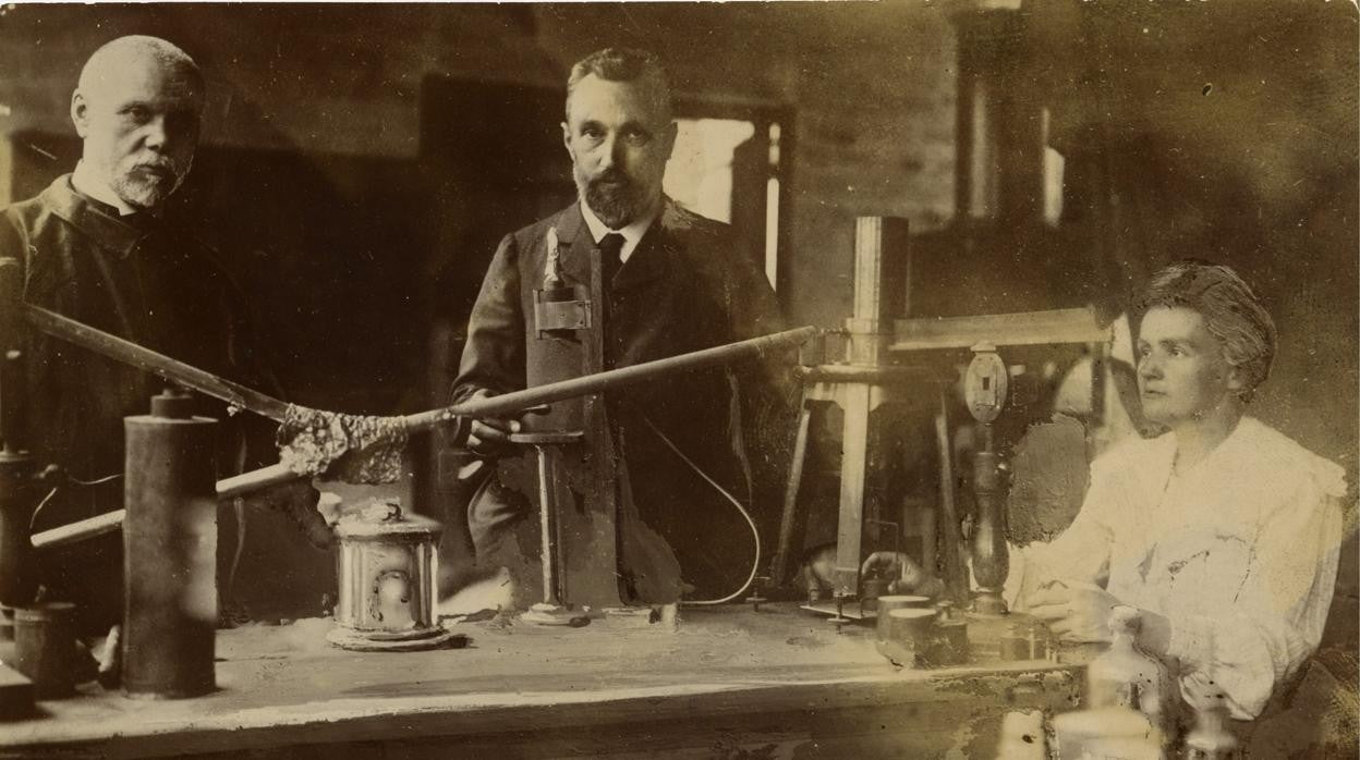 Marie Curie junto a su esposo, en el centro, en su laboratorio, acompañados del químico Gustave Bémont, a la izquierda