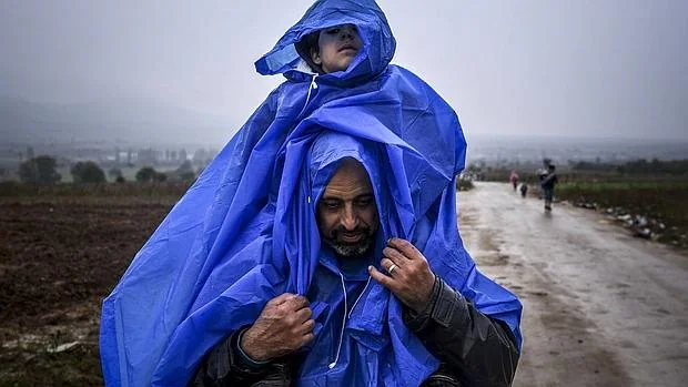 Un refugiado cruza la frontera entre Macedonia y Serbia con su hijo a hombros