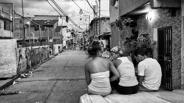 Un grupo de chicas descansa sobre el capó de un viejo coche en la calle real del barrio de Pinto Salinas