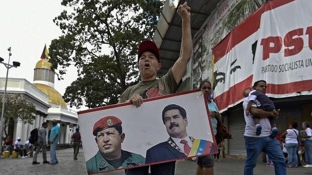 Un seguidor chavista posa con las fotos de Hugo Chávez y Nicolás Maduro