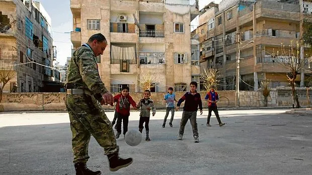 Un miliciano sirio juega al fútbol con unos niños en la ciudad de Alepo