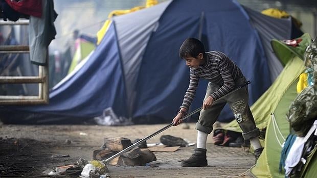 Un niño barre el exterior de su tienda de campaña en el campamento fronterizo griego de Idomeni