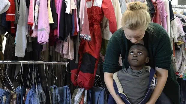 Una trabajadora social viste a un niño refugiado en un centro de recogida de ropa de Munich