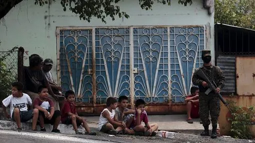 Un grupo de niños salvadoreños junto a un militar que vigila la capital