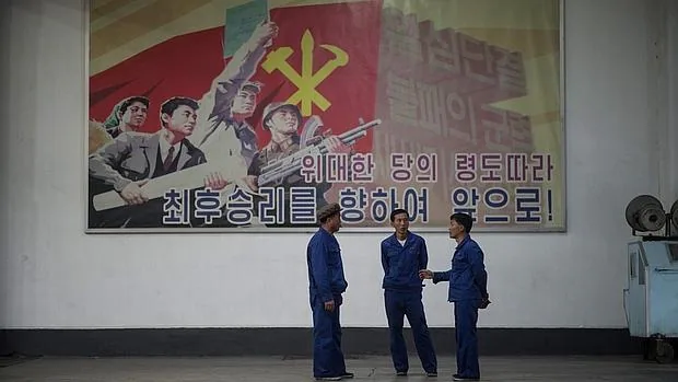 Tres trabajadores junto a un cartel de propaganda del régimen norcoreano, en una fábrica de cable eléctrico de Pyongyang, visitada por periodistas extranjeros