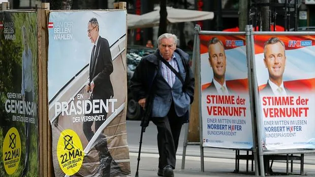 Un hombre camina junto a propaganda electoral de Hofer y de Van der Bellen