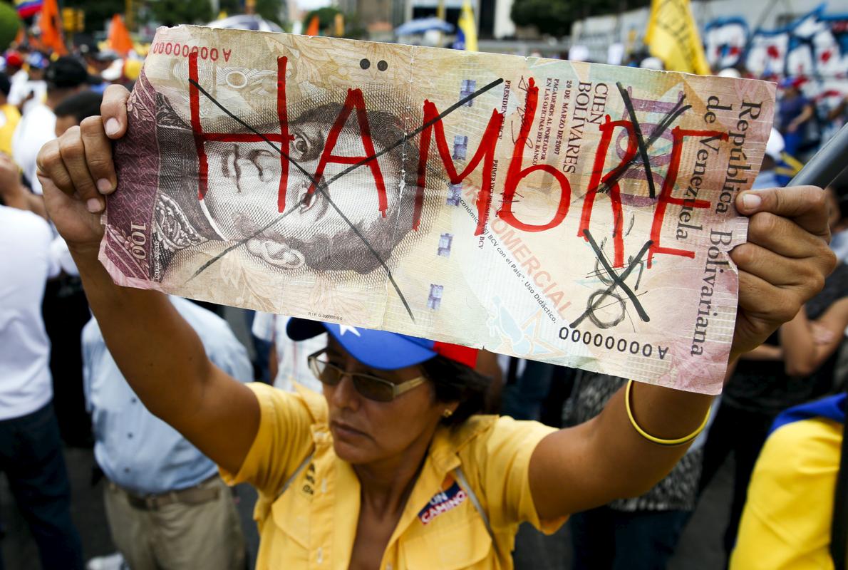 Una mujer sostiene un billete gigante de 100 bolívares en el que pone «Hambre»