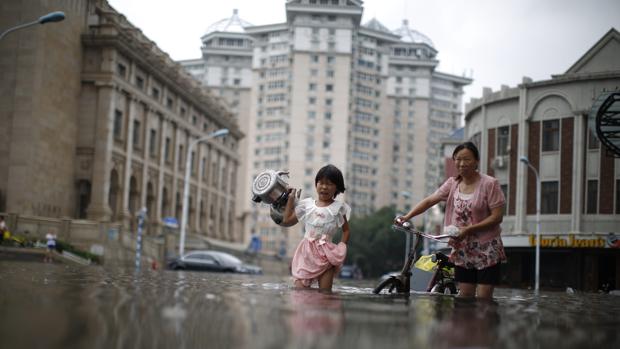 Una madre y su hija pequeña cargada con dos ollas mientras atraviesan una carretera inundada en Tianjin