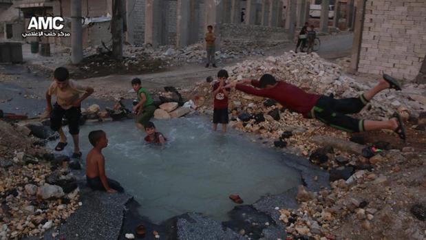 Imagen difundida por activistas sirios en el que varios niños se bañan en el cráter de una bomba en Alepo