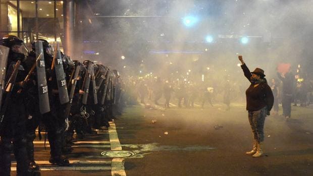 Manifestantes se encaran a policías antidisturbios con los brazos en alto durante unos disturbios en Charlotte en Carolina del Norte