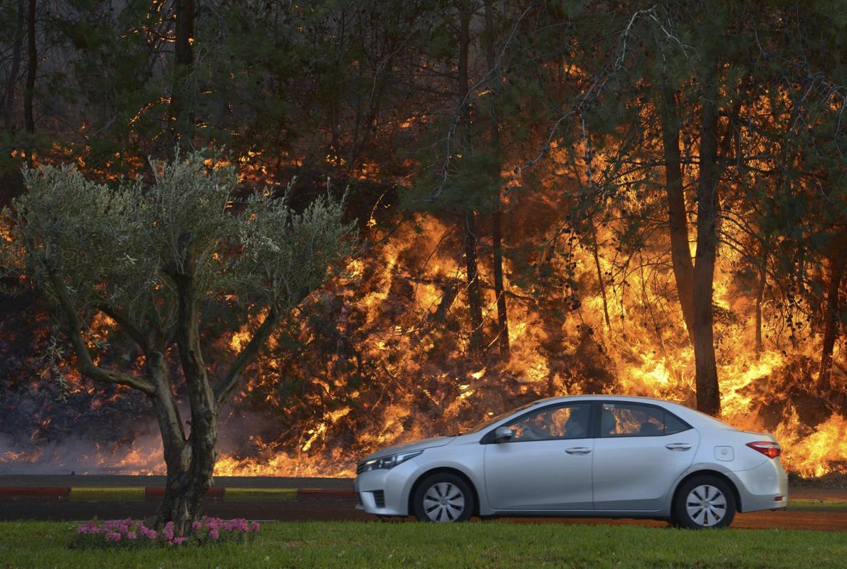 Un coche pasa junto al incendio que comenzó a propagarse cerca de un barrio en la ciudad de Haifa, al norte de Israel,