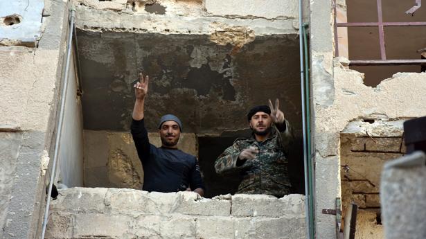 Soldados del Ejército sirio hacen el signo de la victoria desde un edificio destruido por las bombas en Masaken Hanano, una zona del este de Alepo recuperada por las fuerzas de Al Assad