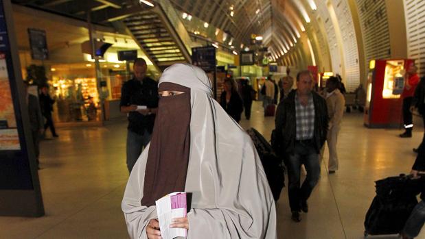Una mujer vestida con un niqab camina por una estación de trenes