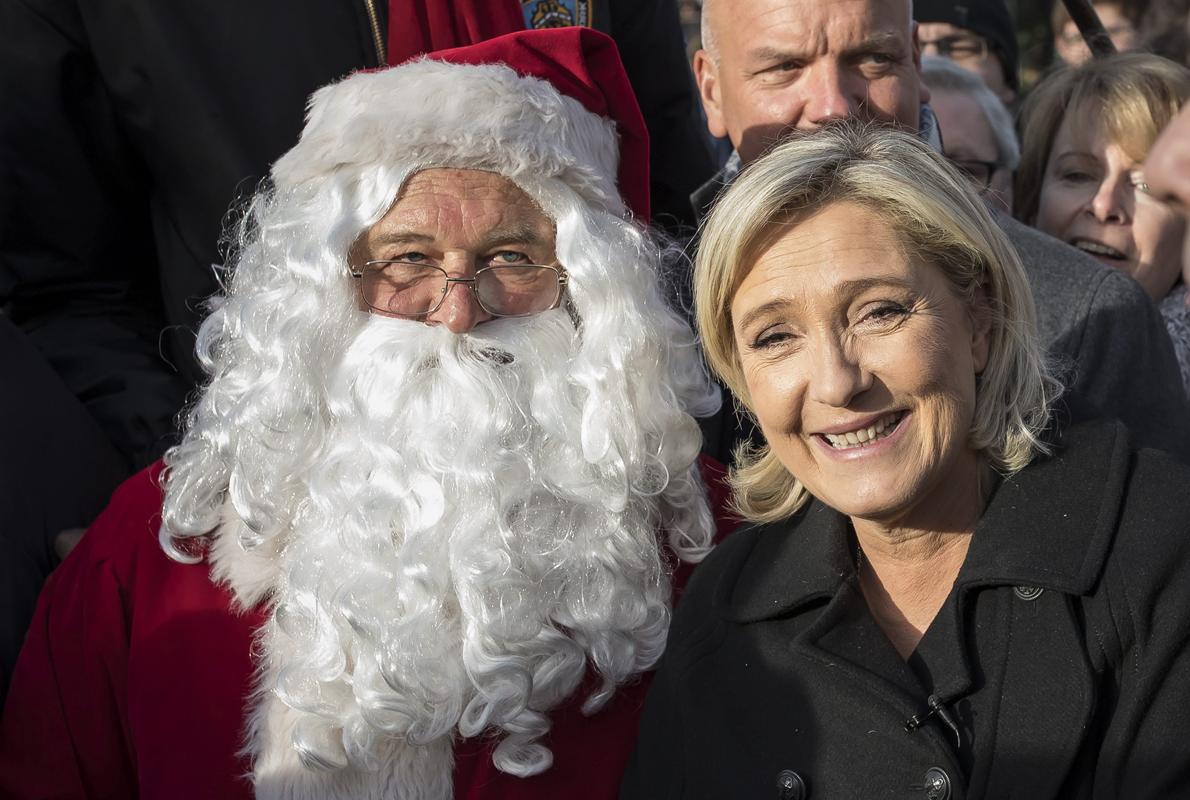 La líder del ultraderechista Frente Nacional (FN) francés, Marine Le Pen (d), posa junto a un papá noel durante una visita a un mercado navideño en los Campos Elíseos en París