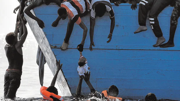 Emigrantes intentan sacar a un bebé del agua, mientras esperan a ser rescatados en el Mediterráneo