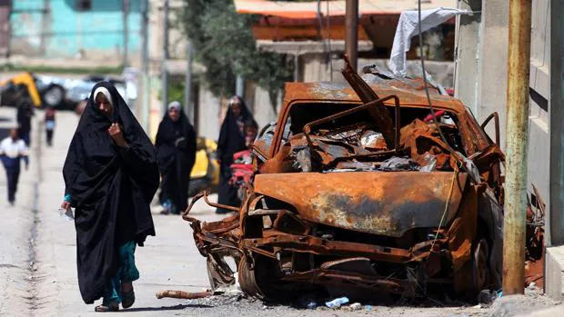 Una mujer camina al lado de un coche destruido por un atentado del Daesh en Irak