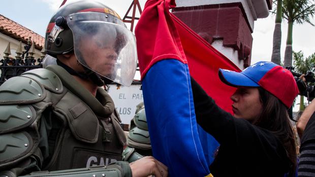 Una mujer sostiene una bandera de Venezuela frente a integrantes de la Guardia Nacional Bolivariana (GNB)