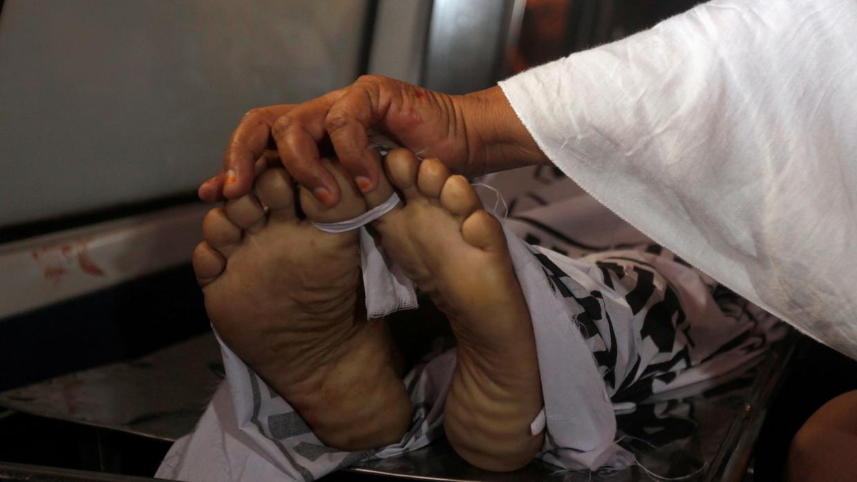 Una madre de un policía, que fue asesinado junto con tres de sus compañeros en un ataque con armas de fuego, toca los pies de su hijo mientras transportaba su cuerpo en una ambulancia fuera de una morgue de un hospital en Karachi, Pakistán