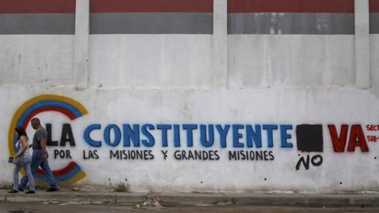 Un pareja camina frente a una pared con propaganda de la Asamblea Nacional Constituyente