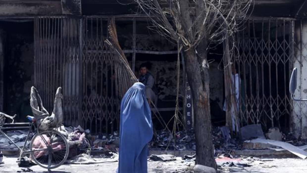 Una mujer ataviada con un burka pasa por delante de un establecimiento destrozado como consecuencia del atentado suicida perpetrado la semana pasada en Kabul