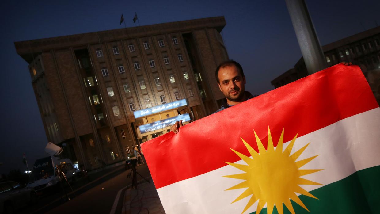 Un hombre posa con la bandera del Kurdistán frente al parlamento kurdo en la ciudad iraquí de Arbil