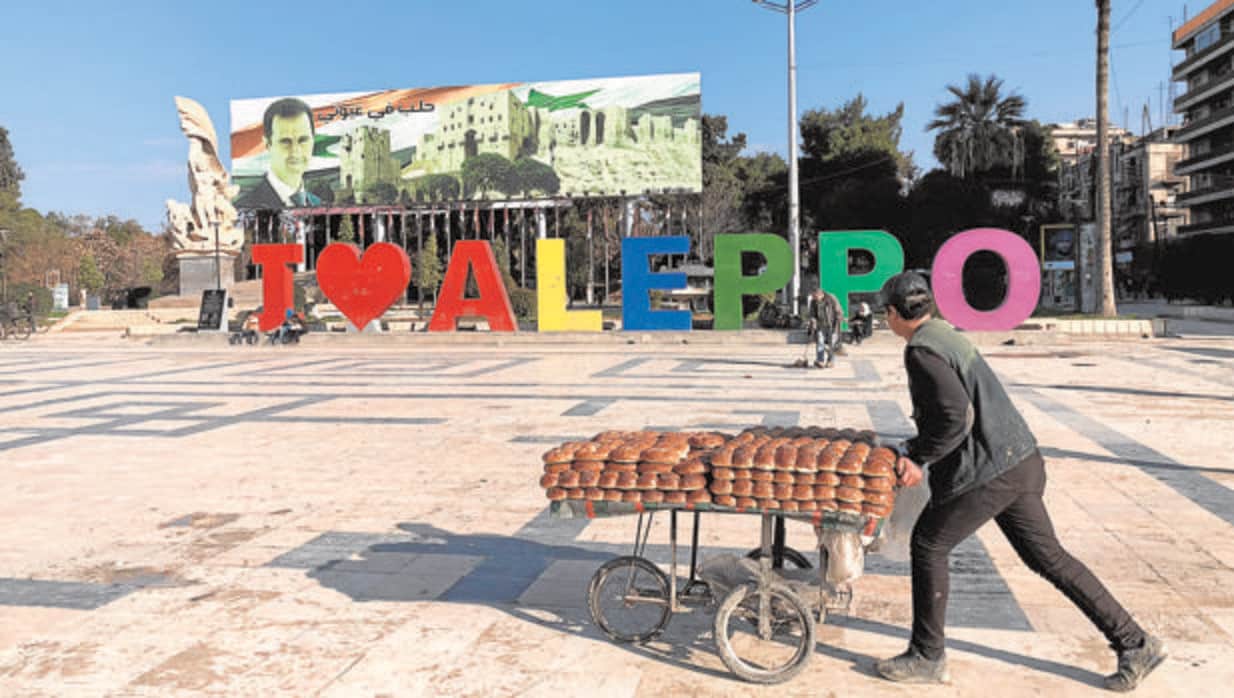 Un vendedor de bollos pasa por delante de un cartel que pone «Yo amo Alepo»