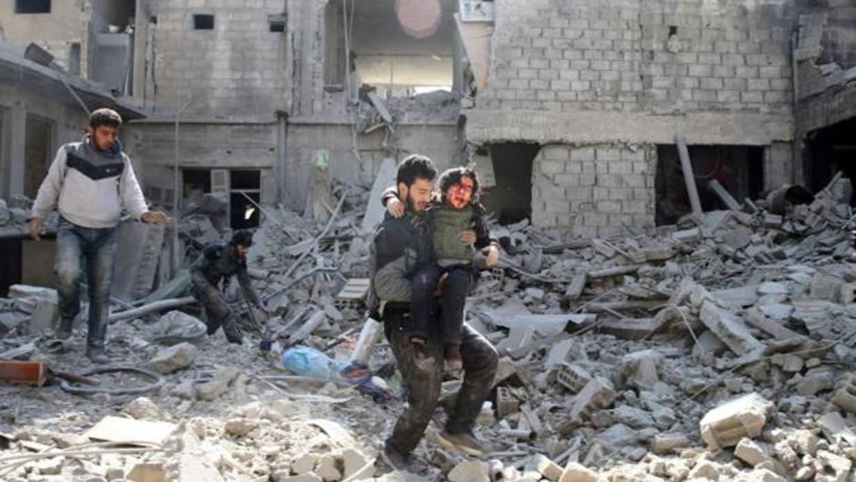 Un hombre lleva en brazos a un chico sobre los escombros de un edificio en Guta, en Siria