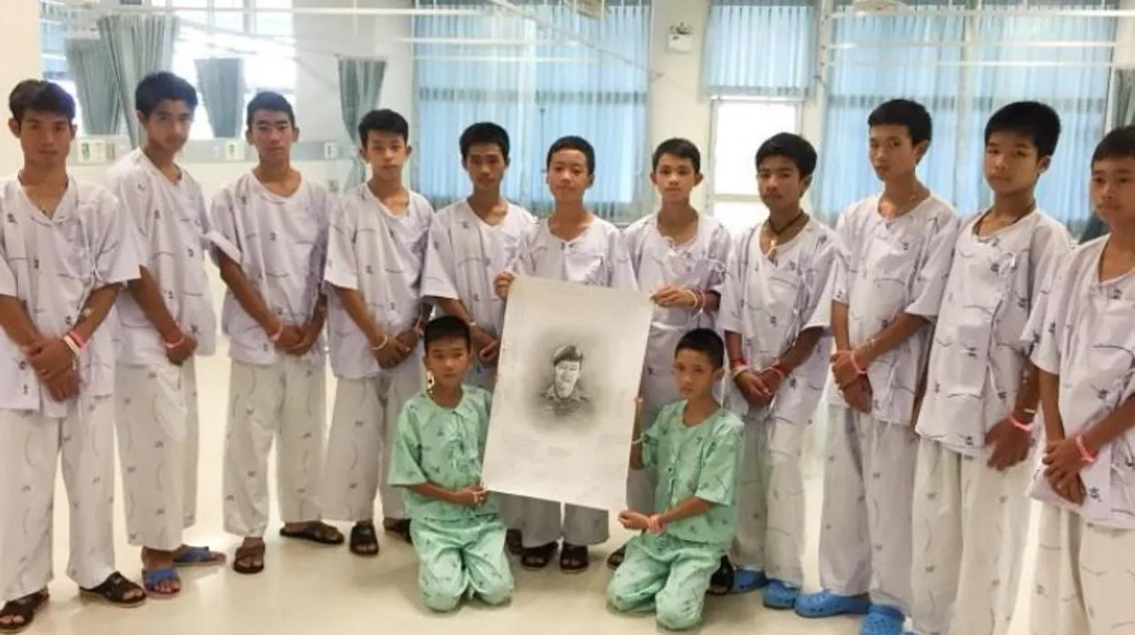 Los chicos atrapados en la cueva de Tailandia junto a una fotografía de Samarn Kunan, el buzo que murió para rescatarles