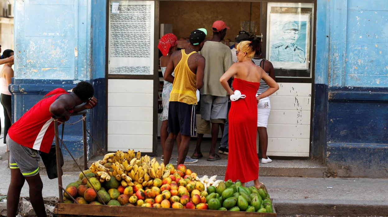 Un hombre empuja un carro de fruta frente a una tienda, donde se aprecia la foto de Raúl Castro