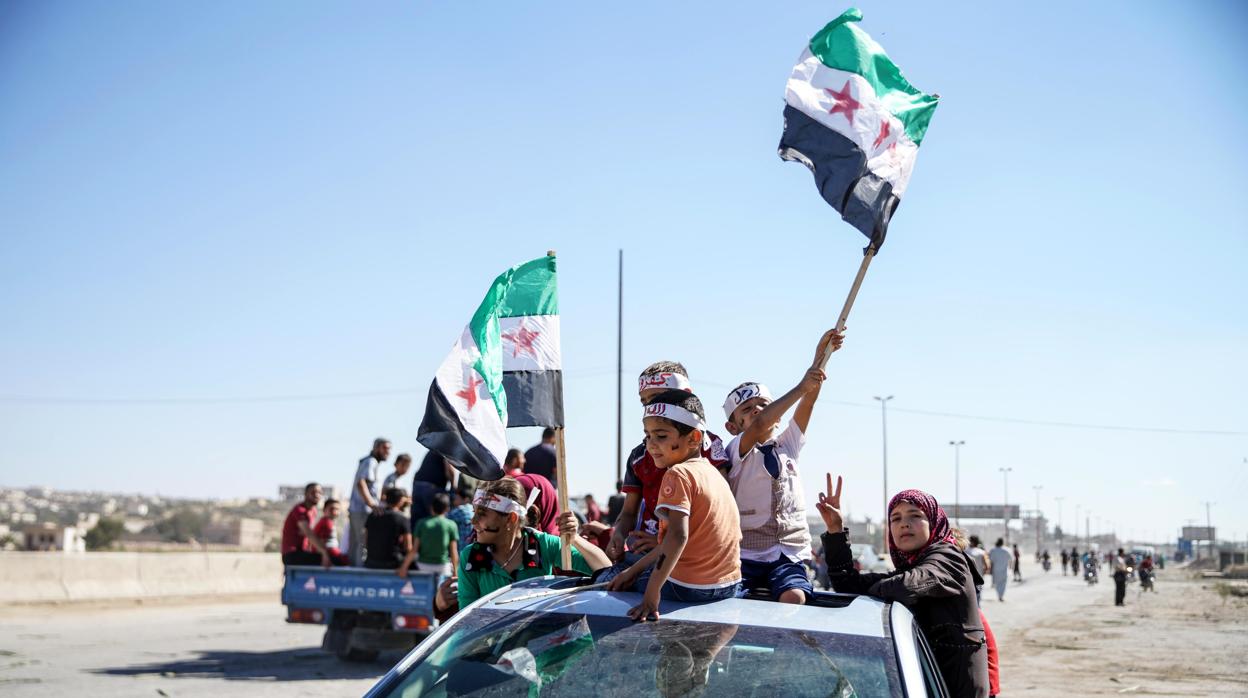 Varias personas ondean banderas sirias revolucionarias durante una protesta en la provincia de Idlib