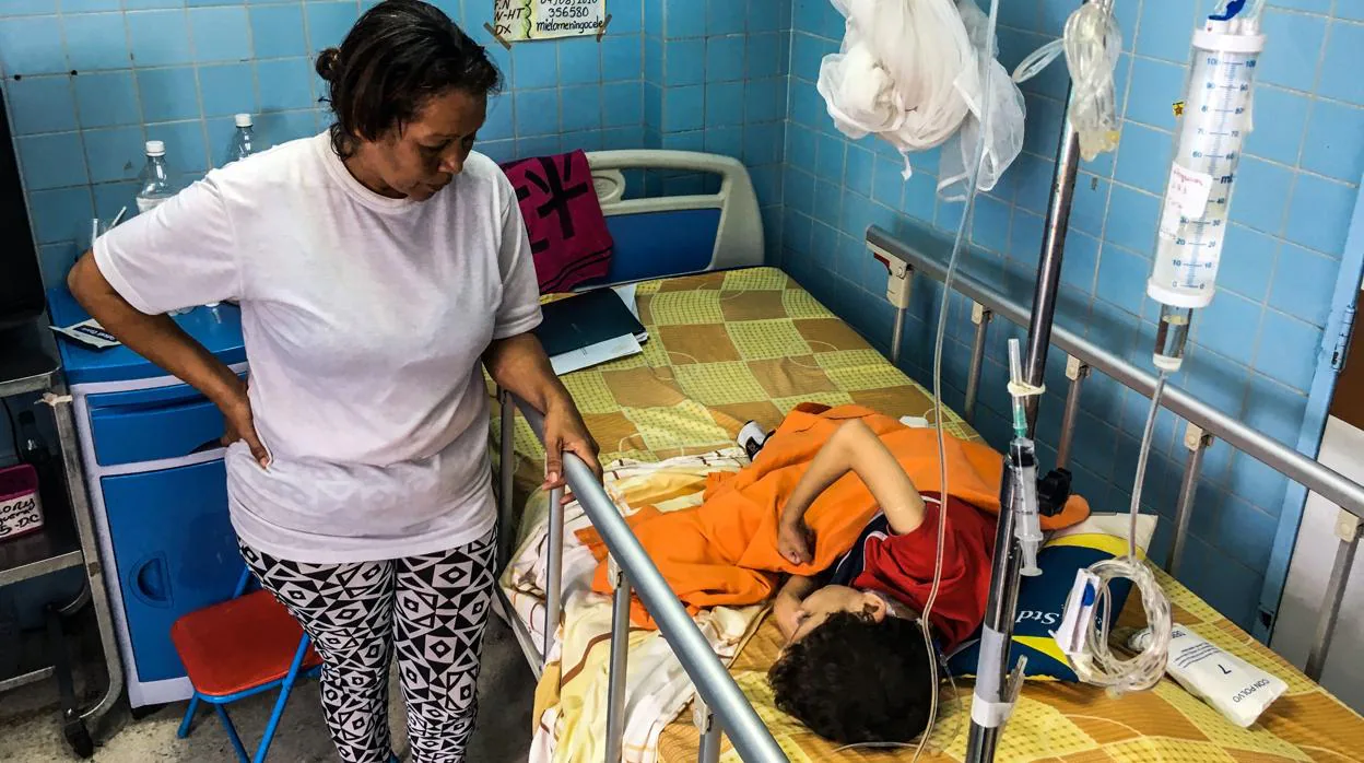 Una mujer está de pie junto a su hijo en la sala de neurocirugía del Hospital de Caracas