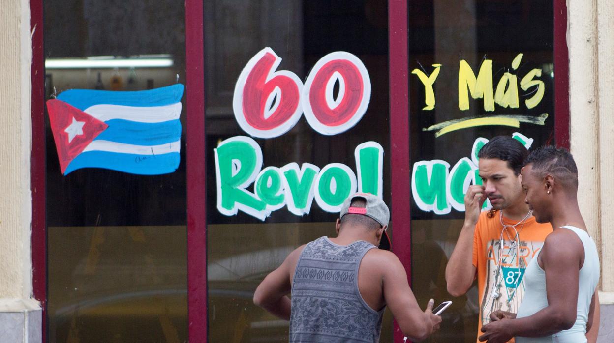 Unos jóvenes conversan frente a una pared con una decoracón alegórica al aniversario del triunfo de la Revolución Cubana, en La Habana