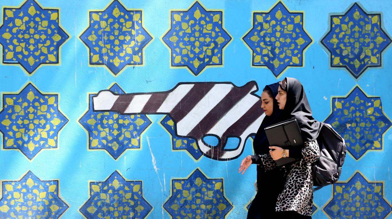 Dos mujeres caminan ante una pintura callejera en un muro de la antigua Embajada de EE.UU. en Teherán