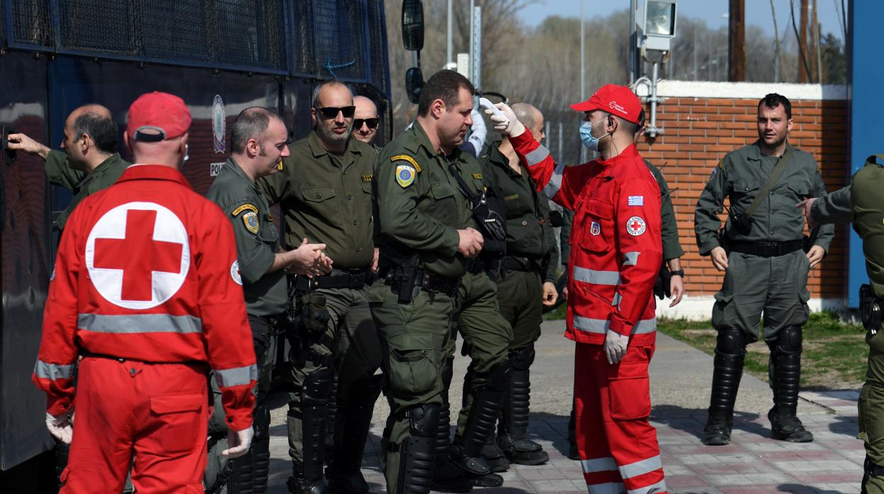 Miembros de la Cruz Roja miden la temperatura a la policía griega que aguarda para entrar en Kastaniés