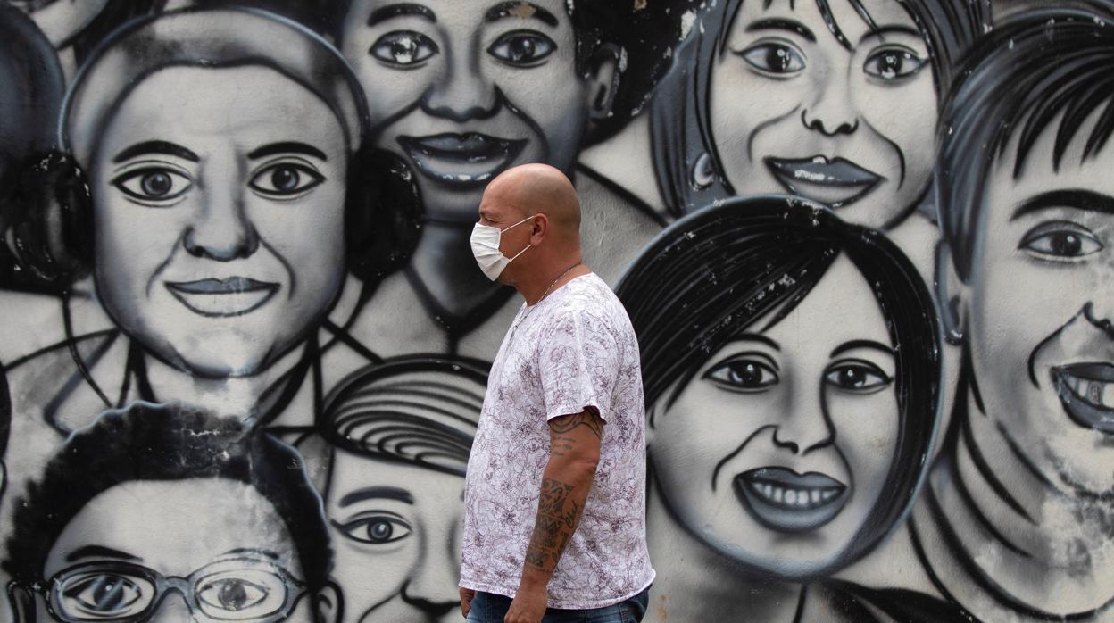 Un hombre con mascarilla camina por delante de un mural en Brasilia (Brasil)