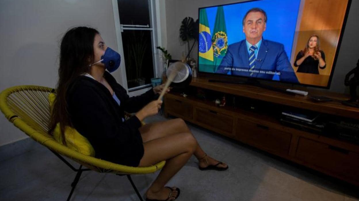 Una mujer con una máscara protesta golpeando una olla durante una declaración televisada del presidente de Brasil, Jair Bolsonaro