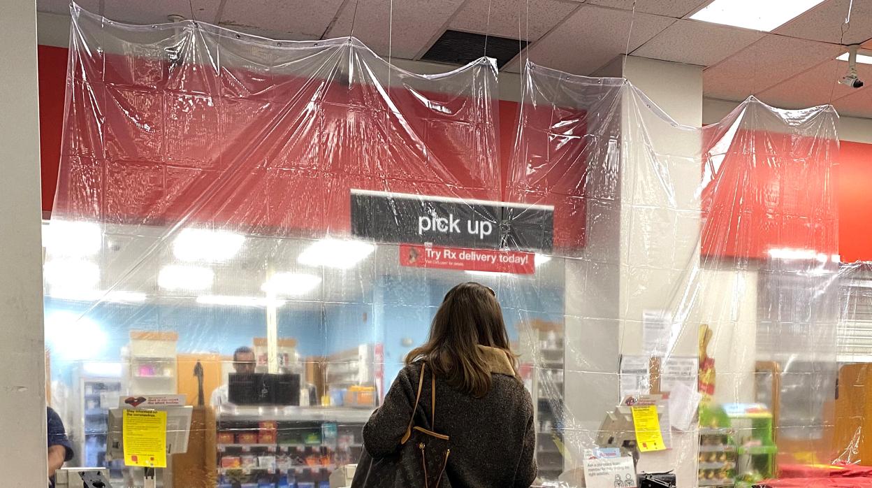 Una mujer es atendida en una farmacia tras un plástico protector