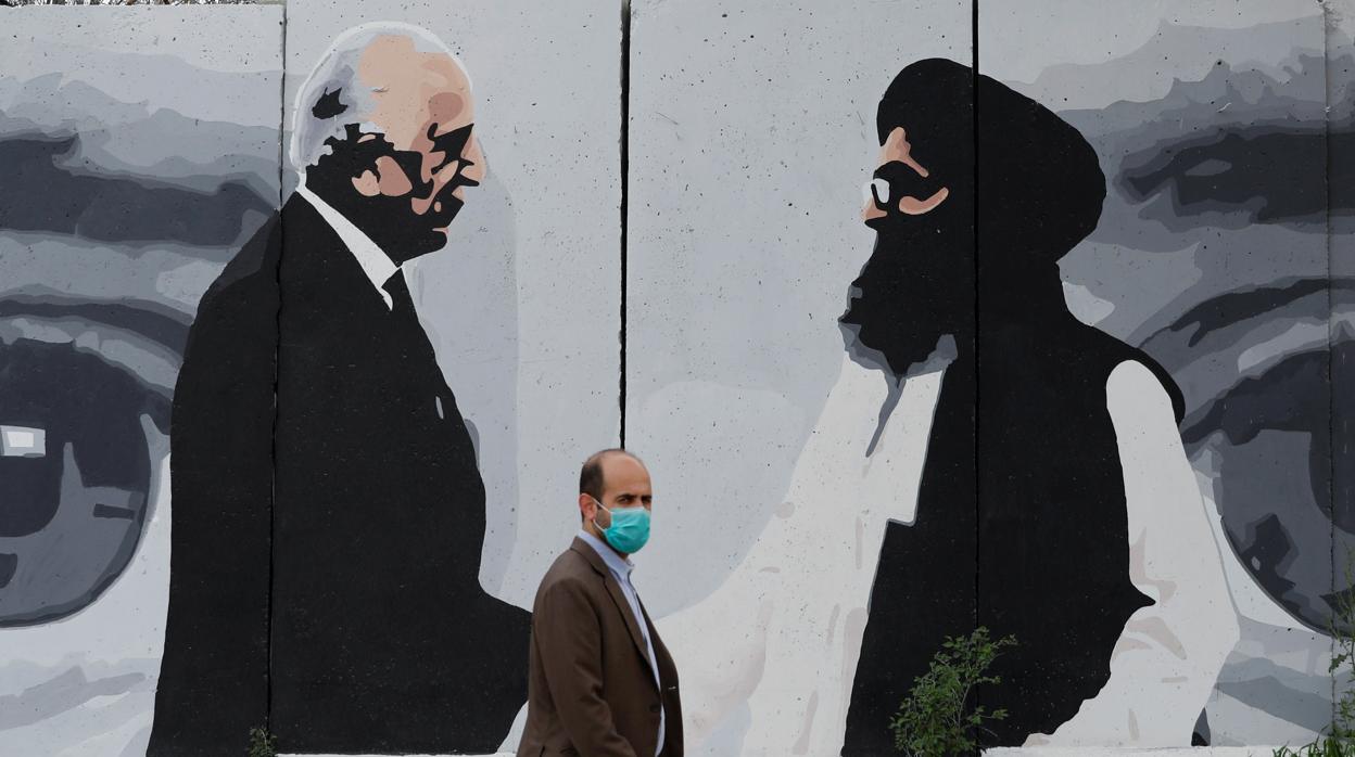 Un ciudadano afgano pasa por delante de un mural en el que aparece el enviado de EE.UU. para las negociaciones de paz Zalmay Khalilzad, y Ghani, líder de la delegación talibán