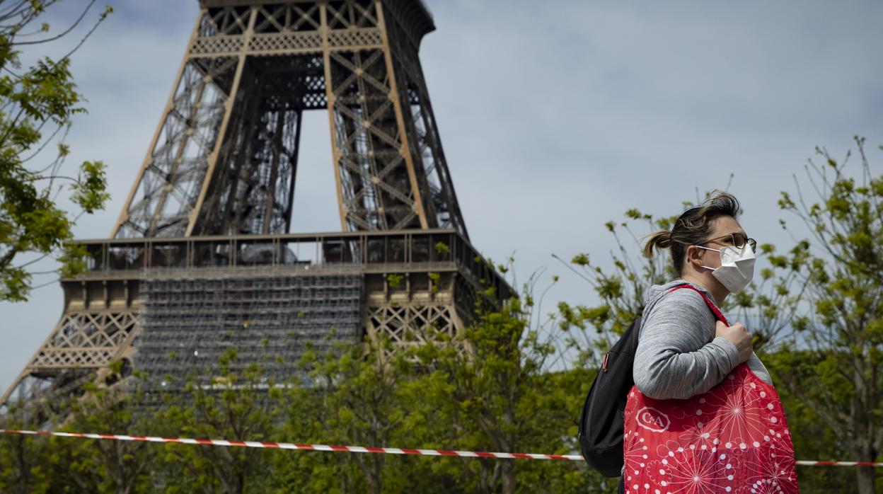 Una mujer con mascarilla pasa por un cordón policial cerca de la torre Eiffel durante el confinamiento