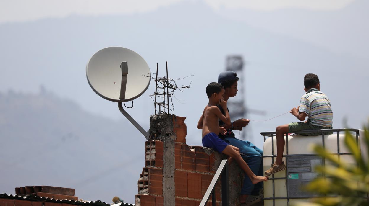 Unos niños juegan cerca de una antena de Directv en un barrio popular de Caracas