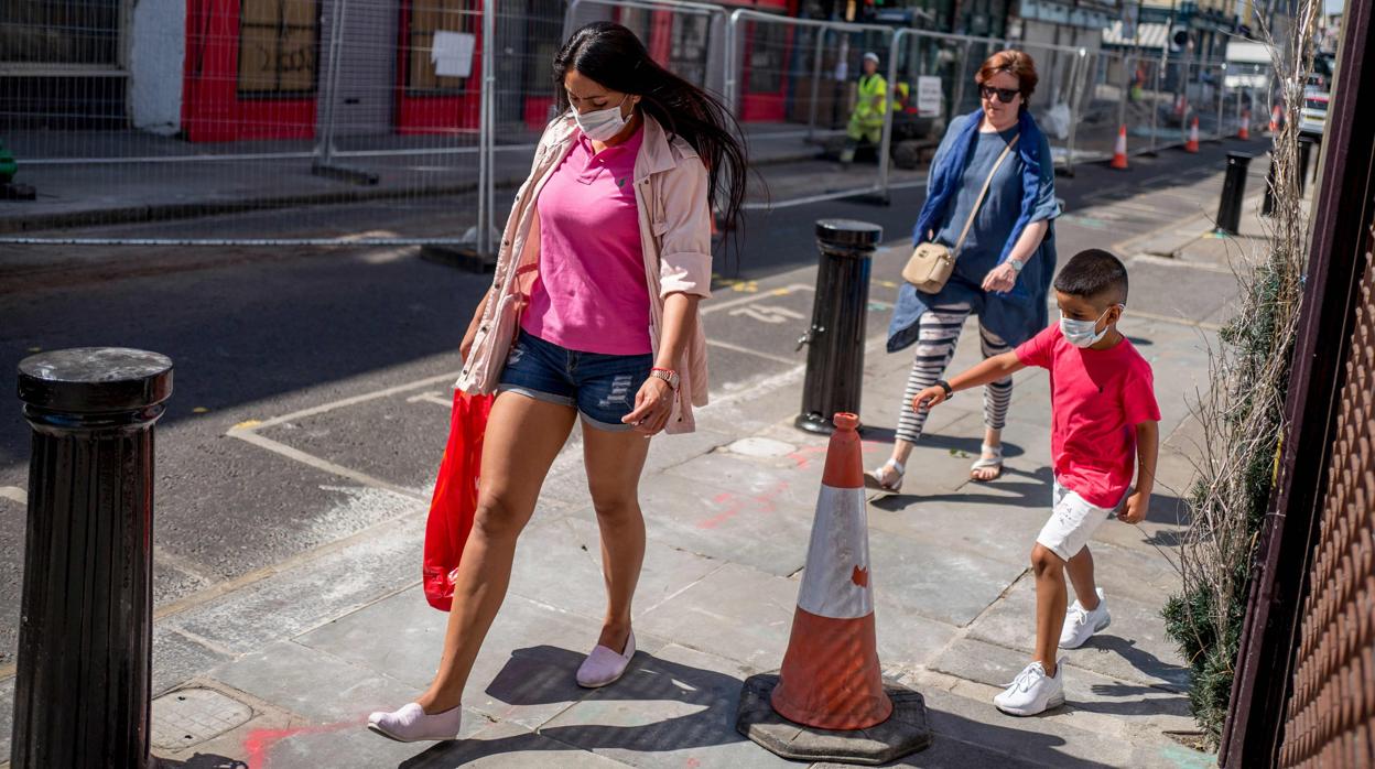 Una mujer y un niño pasean protegidos con mascarillas por las calles de Londres