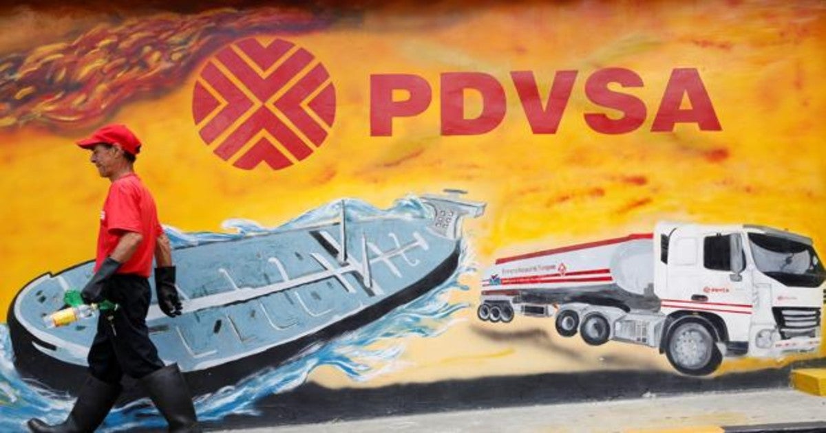 Un trabajador pasa frente a un mural con el logotipo de Pdvsa, en su estación de servicio en Caracas